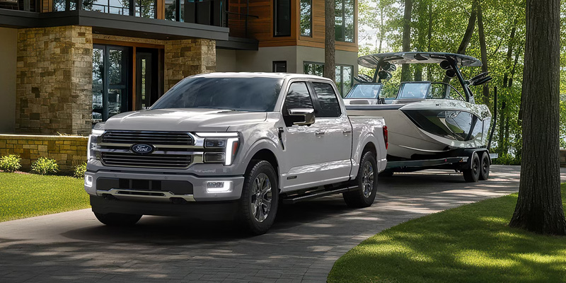 White Ford F-150 towing a wake boat in a residential driveway.