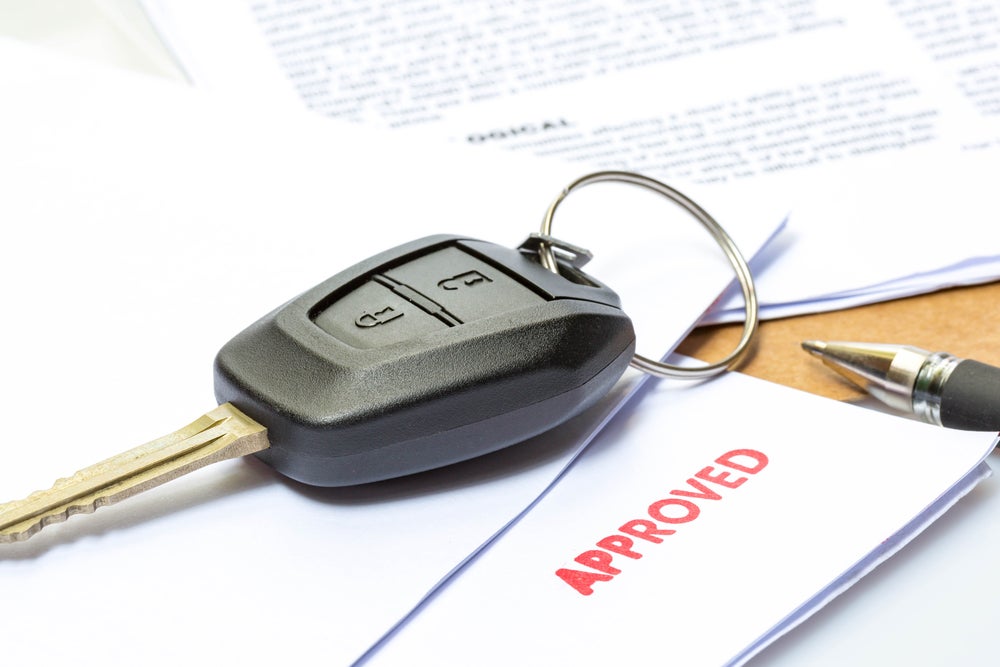 Car key placed on approved vehicle financing documents with a pen on a desk.