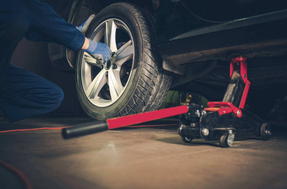 Mechanic removing a vehicle tire with a jack and tools during auto repair service.